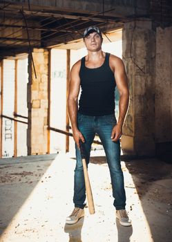 Muscular man with baseball bat on the ruins