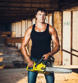 Muscular man with a chainsaw on the ruins