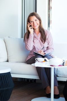 Happy businesswoman talking on the phone and writing in organizer in a coffee shop