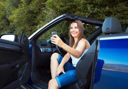 Smiling caucasian woman with cellphone in a cabriolet car