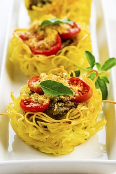 pasta nest arranged on a white porcelain plate with tomatoes parmesan and some leaves of basil