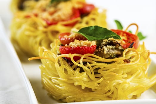 pasta nest arranged on a white porcelain plate with tomatoes parmesan and some leaves of basil