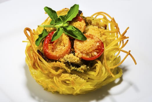 pasta nest arranged on a white porcelain plate with tomatoes parmesan and some leaves of basil