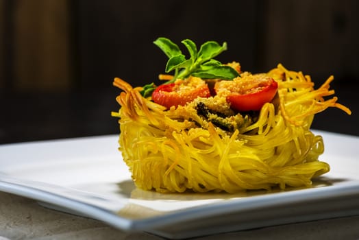 pasta nest arranged on a white porcelain plate with tomatoes parmesan and some leaves of basil