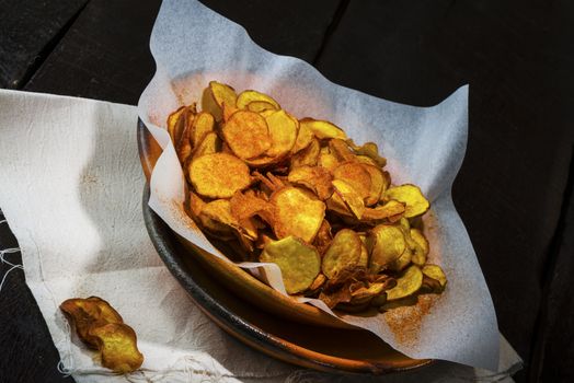 Homemade sweet potatoes chips in a rustic clay plate on wood table