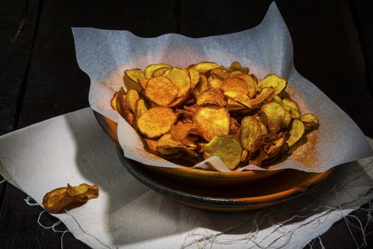 Homemade sweet potatoes chips in a rustic clay plate on wood table