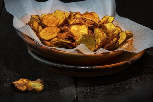 Homemade sweet potatoes chips in a rustic clay plate on wood table