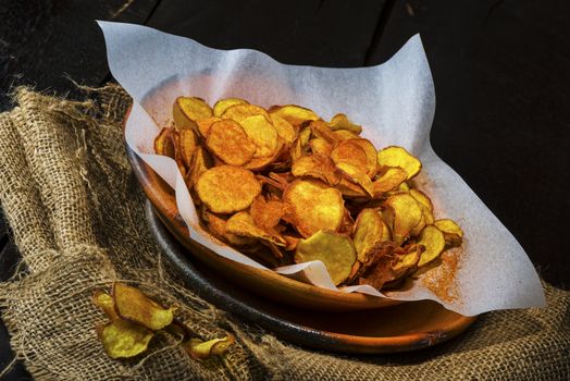 Homemade sweet potatoes chips in a rustic clay plate on wood table