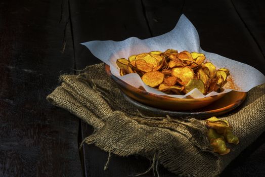 Homemade sweet potatoes chips in a rustic clay plate on wood table