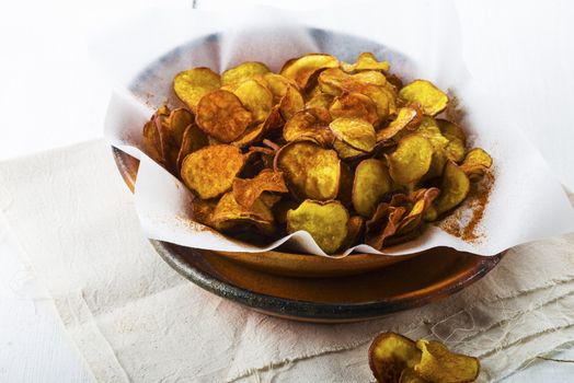 Homemade sweet potatoes chips in a rustic clay plate on white wood table