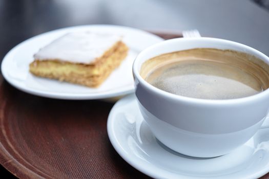 Shallow depth of field shot of coffee cup with mille feuille in the blurred background