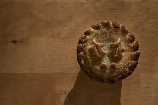 Single mince pie shot directly from above on wooden table, with lots of copy space