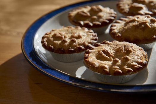 Plate of mince pies shot against the light on a wooden table