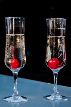 two glasses filled with sparkling wines and each of them with a cherrie inside standing on a counter top.