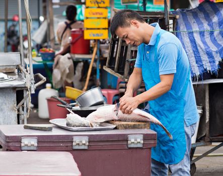 PATTAYA, THAILAND - NOVEMBER 27, 2014: Market vendor slicing a fish before opening his restaurant at an outdoor market in Pattaya City.