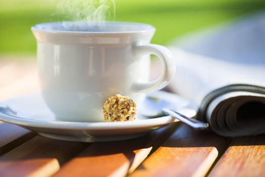 a white cup of hot coffee on wood table with newspaper and area for your text