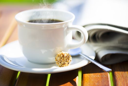 a white cup of hot coffee on wood table with newspaper and area for your text