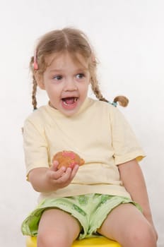 Three year old girl with pigtails and funny enthusiastically eating a bun