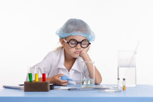 Chemist girl sitting at the table with the reagents in chemistry class and puts experiments