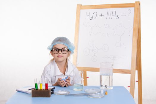 Chemist girl sitting at the table with the reagents in chemistry class and puts experiments