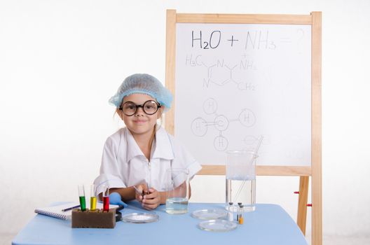 Chemist girl sitting at the table with the reagents in chemistry class and puts experiments