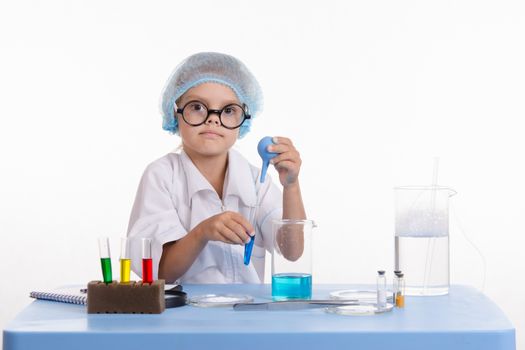 Chemist girl sitting at the table with the reagents in chemistry class and puts experiments