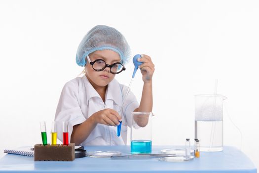 Chemist girl sitting at the table with the reagents in chemistry class and puts experiments