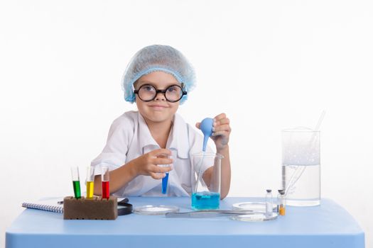 Chemist girl sitting at the table with the reagents in chemistry class and puts experiments