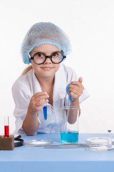 Chemist girl sitting at the table with the reagents in chemistry class and puts experiments