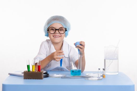 Chemist girl sitting at the table with the reagents in chemistry class and puts experiments