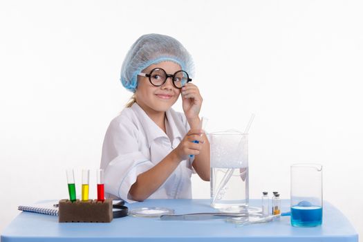 Chemist girl sitting at the table with the reagents in chemistry class and puts experiments