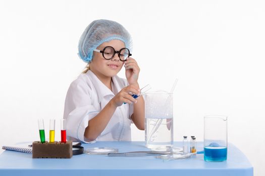 Chemist girl sitting at the table with the reagents in chemistry class and puts experiments