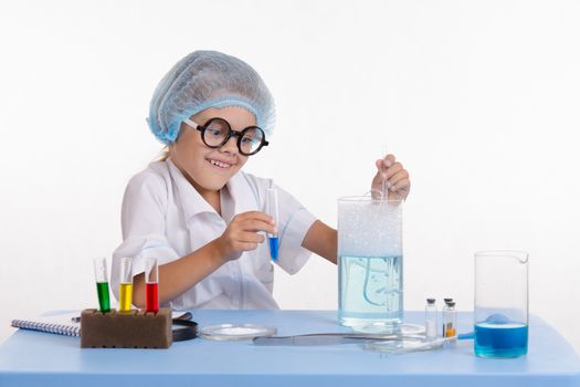 Chemist girl sitting at the table with the reagents in chemistry class and puts experiments