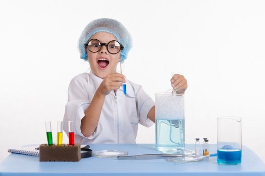 Chemist girl sitting at the table with the reagents in chemistry class and puts experiments