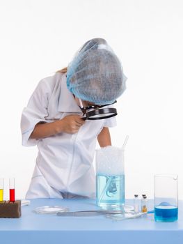 Chemist girl sitting at the table with the reagents in chemistry class and puts experiments