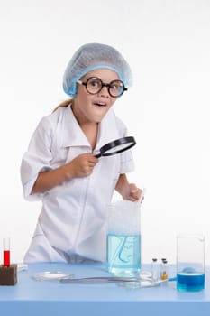 Chemist girl sitting at the table with the reagents in chemistry class and puts experiments