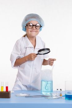 Chemist girl sitting at the table with the reagents in chemistry class and puts experiments