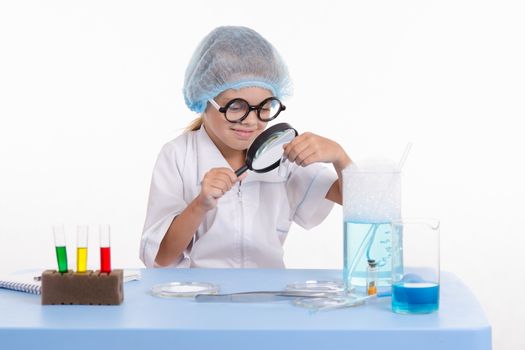 Chemist girl sitting at the table with the reagents in chemistry class and puts experiments