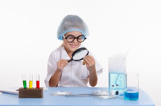 Chemist girl sitting at the table with the reagents in chemistry class and puts experiments