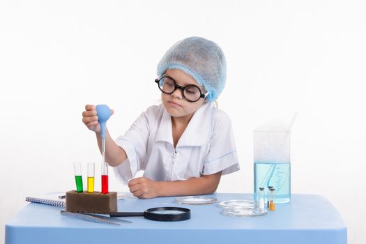 Chemist girl sitting at the table with the reagents in chemistry class and puts experiments