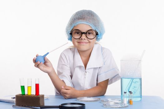 Chemist girl sitting at the table with the reagents in chemistry class and puts experiments