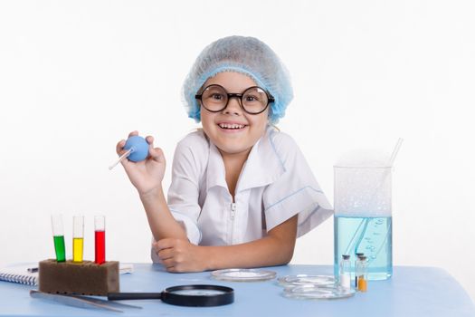 Chemist girl sitting at the table with the reagents in chemistry class and puts experiments