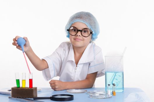 Chemist girl sitting at the table with the reagents in chemistry class and puts experiments