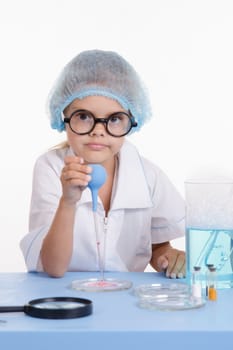 Chemist girl sitting at the table with the reagents in chemistry class and puts experiments