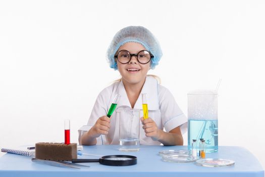 Chemist girl sitting at the table with the reagents in chemistry class and puts experiments