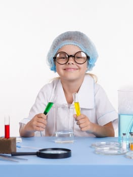 Chemist girl sitting at the table with the reagents in chemistry class and puts experiments
