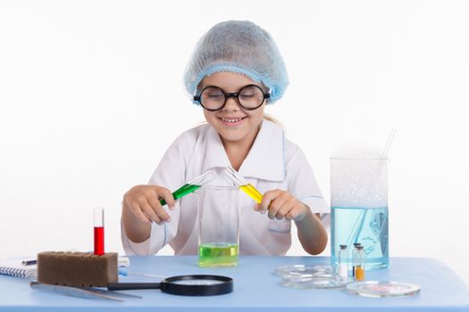 Chemist girl sitting at the table with the reagents in chemistry class and puts experiments