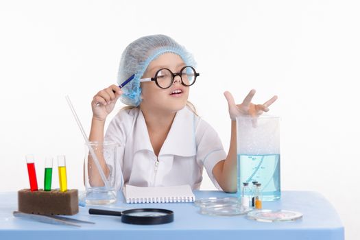 Chemist girl sitting at the table with the reagents in chemistry class and puts experiments