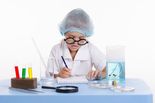 Chemist girl sitting at the table with the reagents in chemistry class and puts experiments