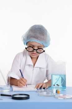 Chemist girl sitting at the table with the reagents in chemistry class and puts experiments